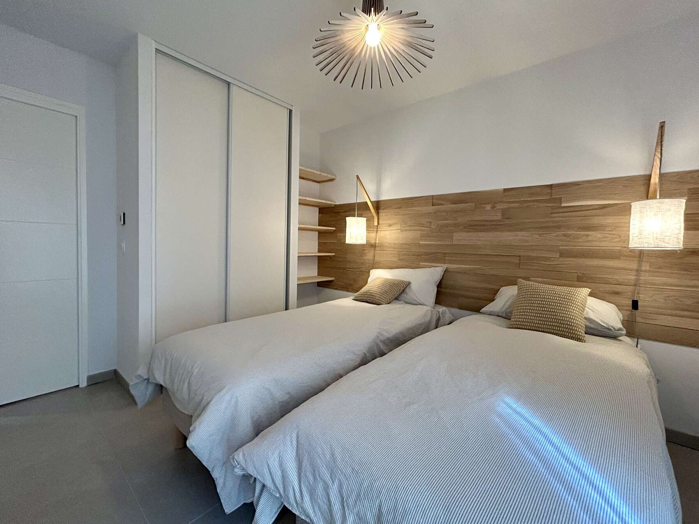 Et moderne soveværelse med to senge, en træsengegavl og en loftlampe.