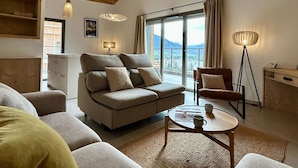 A modern living room with a sofa, a coffee table, and a floor lamp. There is a large window with a view of the outdoors.