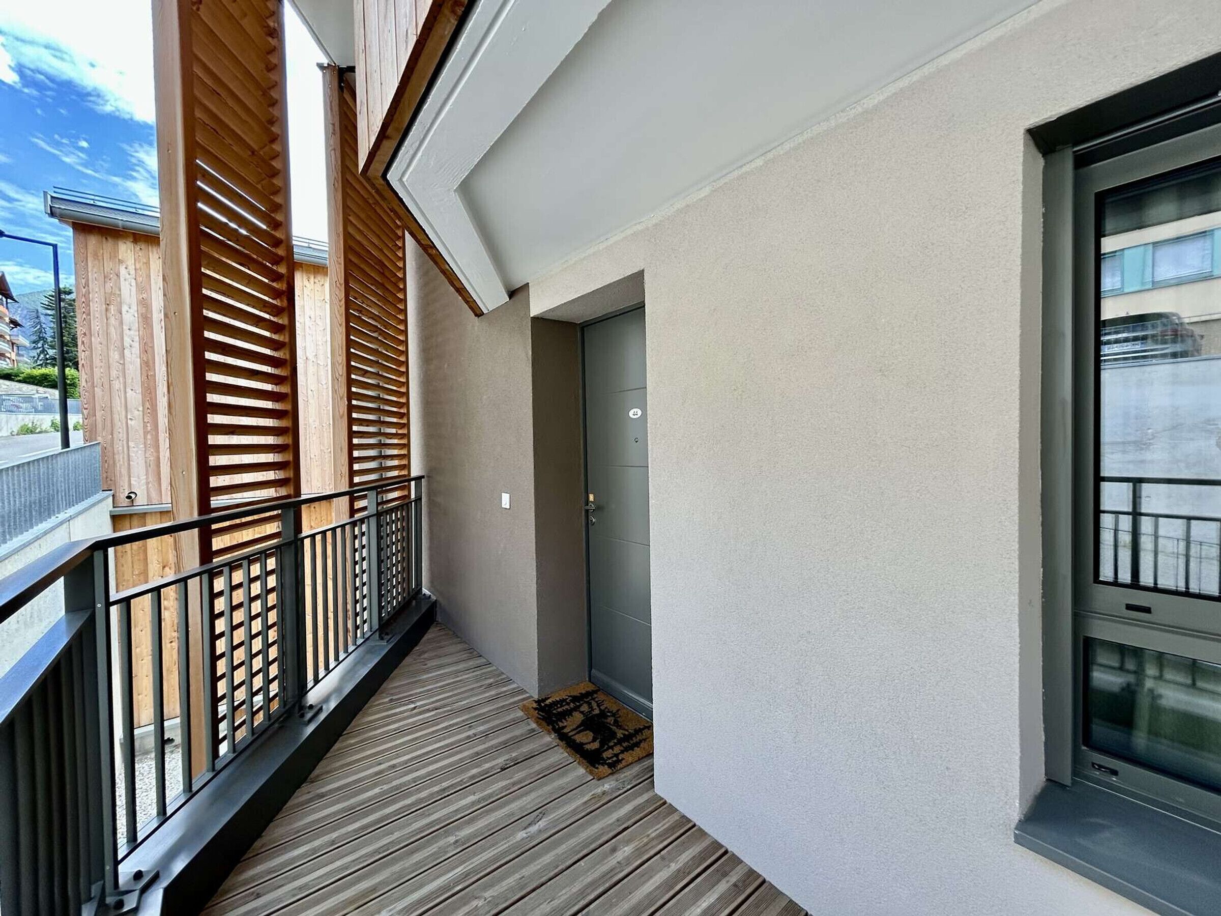 Ein Balkon mit Holzlatten, einem Metallgeländer und einer Tür zu einem Innenraum.