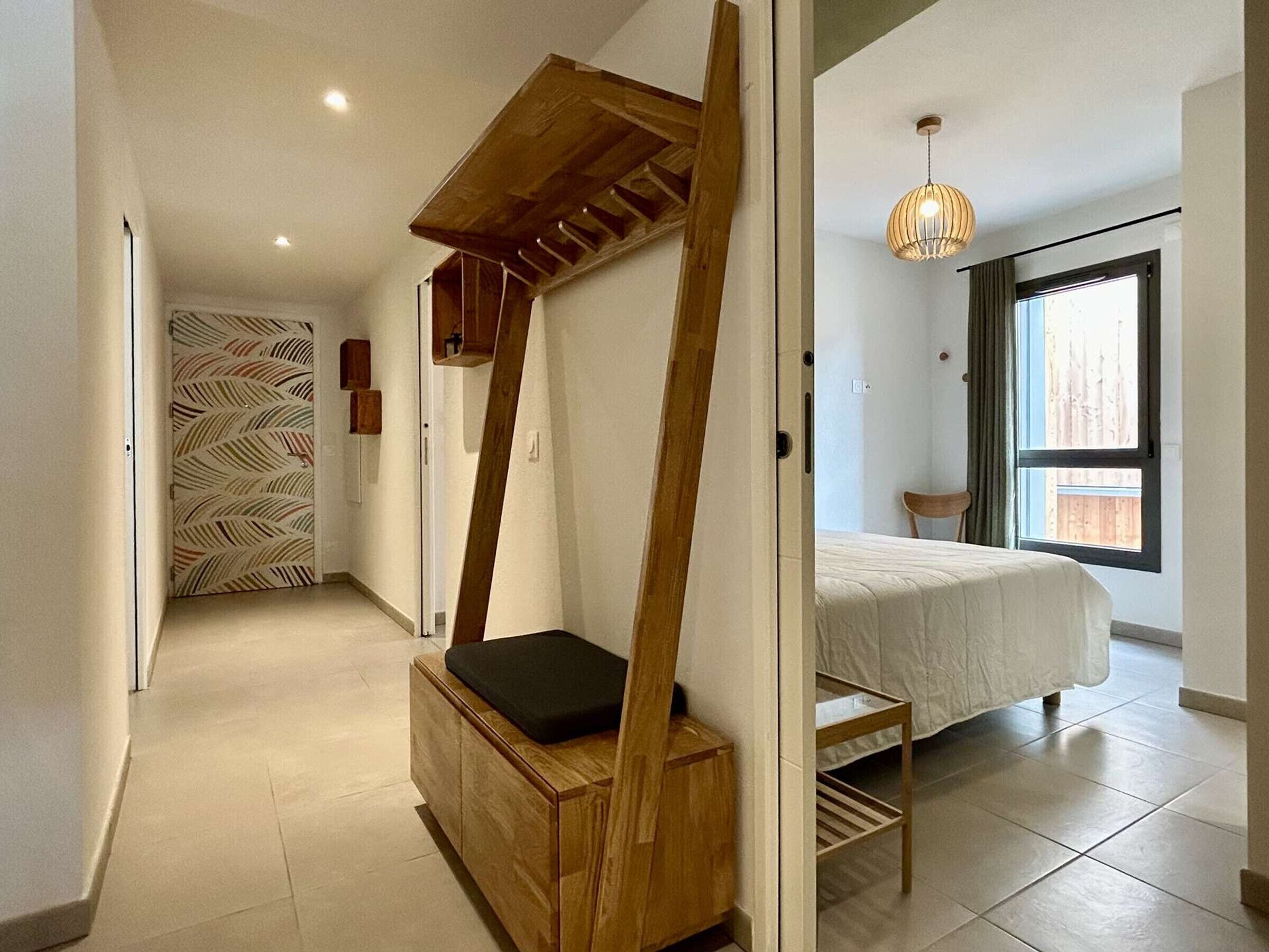 Ein Schlafzimmer mit einem Bett, einer hölzernen Bank, einer Pendelleuchte, einem Fenster und einer Wand mit Muster.