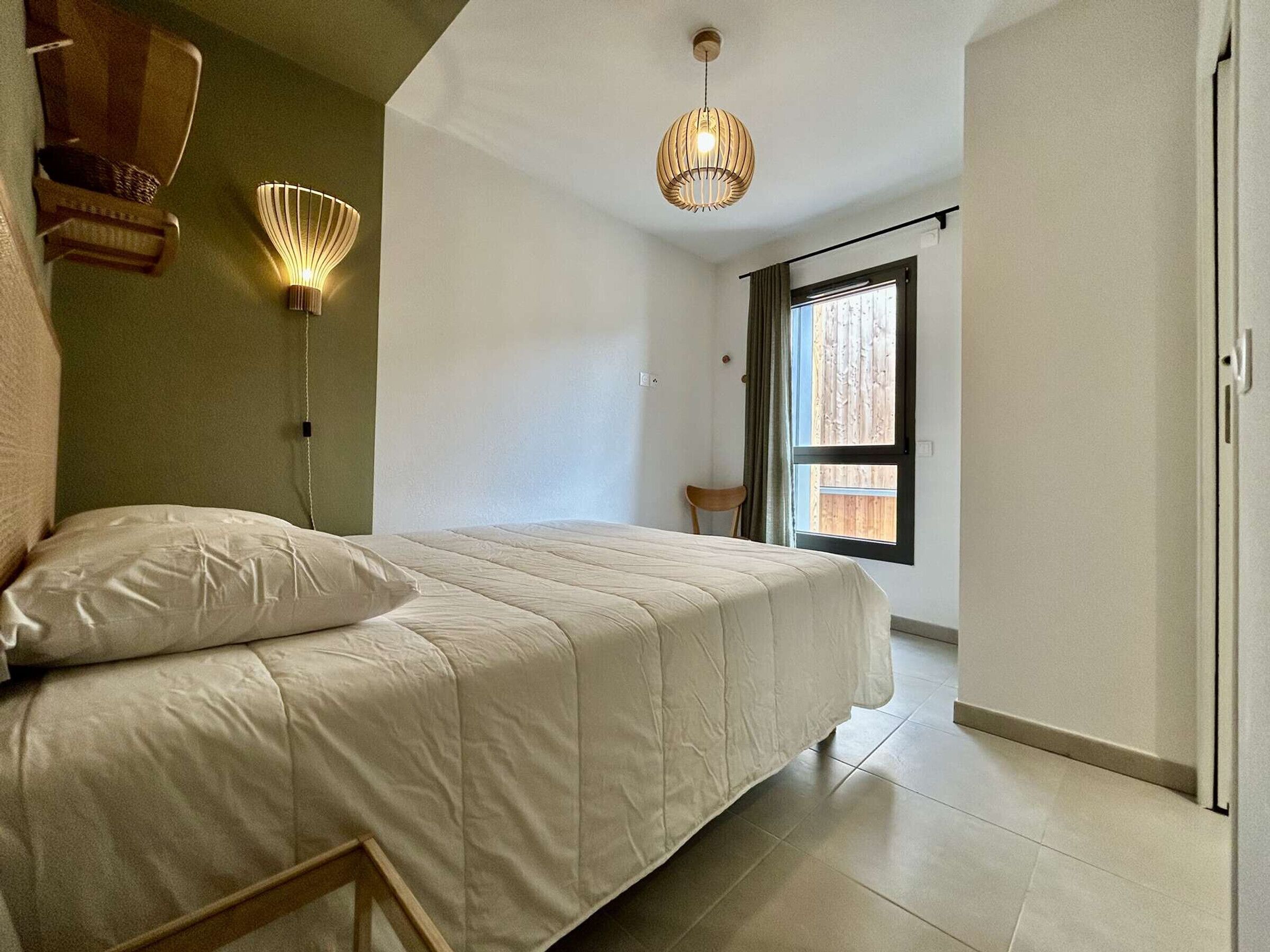 Ein Schlafzimmer mit einem Bett, einem Sessel, einem Kleiderschrank und einem Fenster mit Vorhängen.