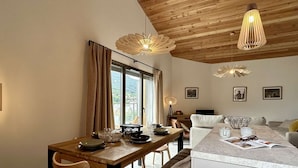 A modern kitchen with a dining area, wooden ceiling, and large windows.