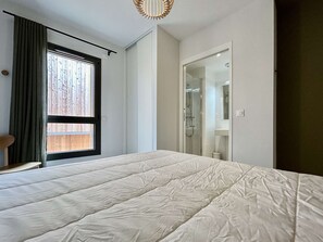 A bedroom with a bed, a window with curtains, a door leading to a bathroom, and a chair.