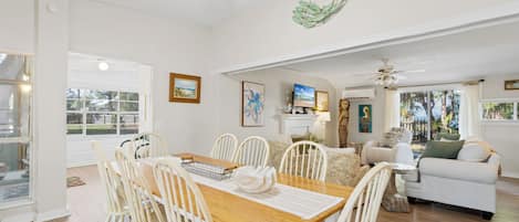 A spacious living room with a wooden dining table, white chairs, a white sofa, and a ceiling fan.