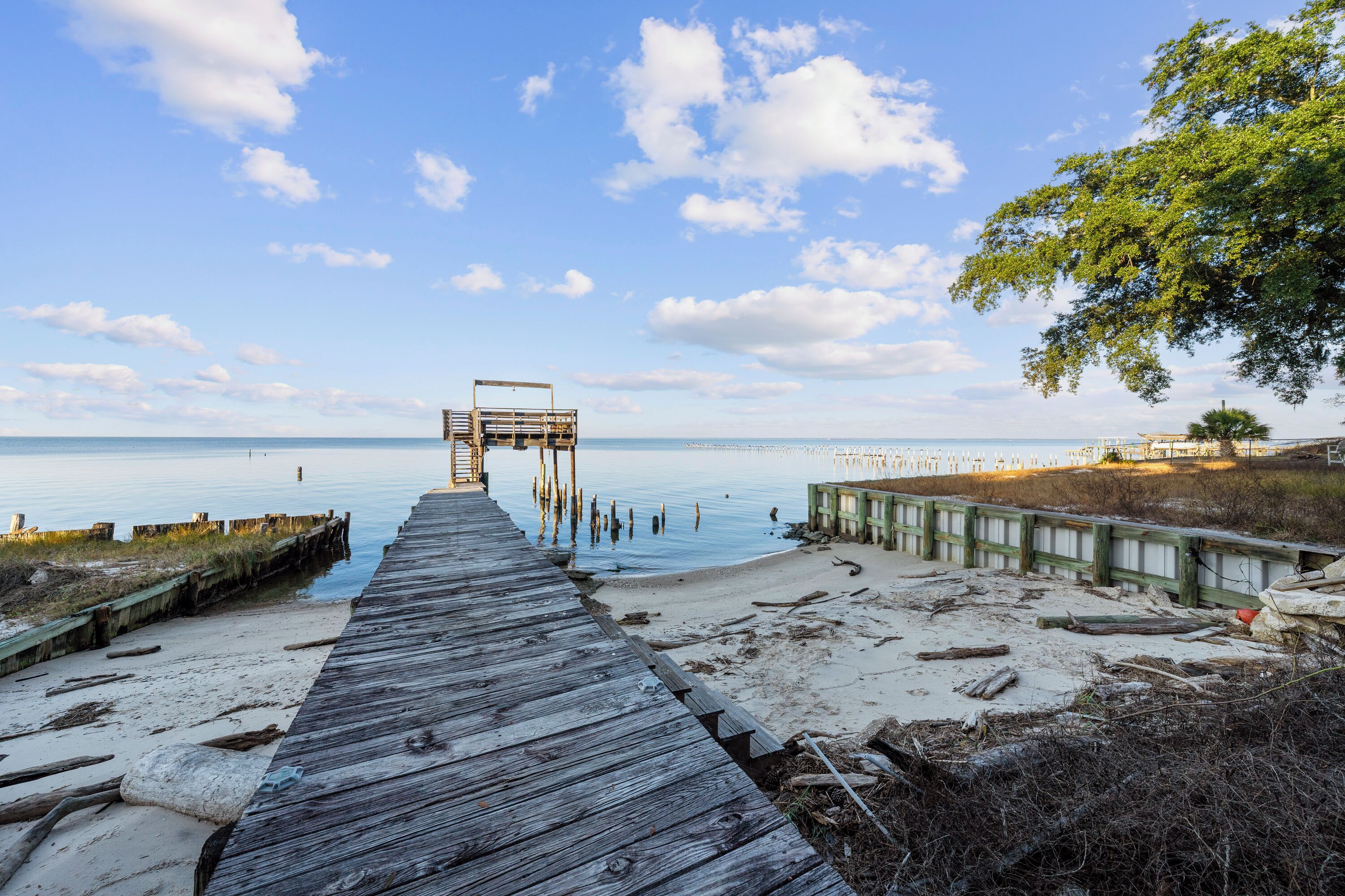 Eine hölzerne Pier führt zu einem Strand, am Ende befindet sich ein Holzgebäude.