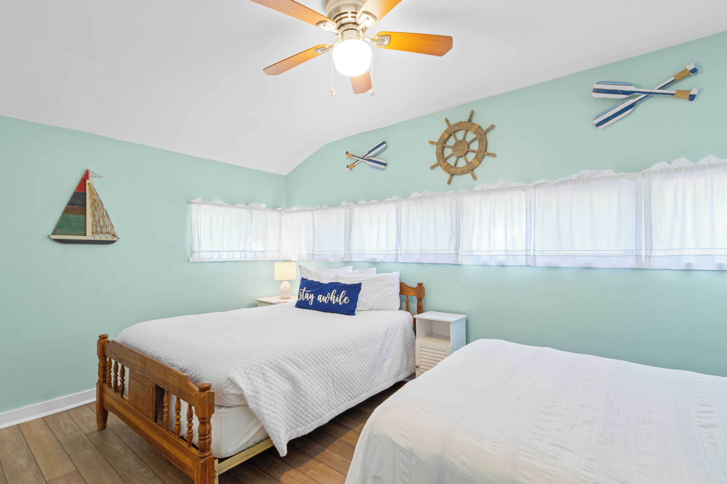 Ein Schlafzimmer mit Bett, Nachttisch, Deckenventilator und Wanddekorationen im maritimen Stil.