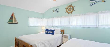 Ein Schlafzimmer mit Bett, Nachttisch, Deckenventilator und Wanddekorationen im maritimen Stil.