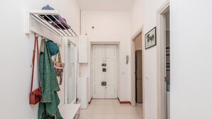 Un couloir étroit avec un banc, un porte-manteau sur lequel sont suspendus des vêtements, et une porte au fond.