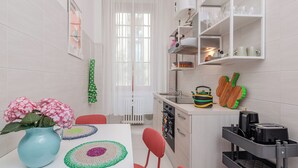 Une cuisine moderne avec des meubles blancs, un four encastré et un évier. On peut voir un vase avec des fleurs sur le comptoir et un set de table coloré en fibres tressées.