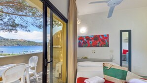A hotel room with a bed, a desk with chairs, a painting, and a view of the sea. - Hotel in Capoliveri with private beach (Capoliveri)