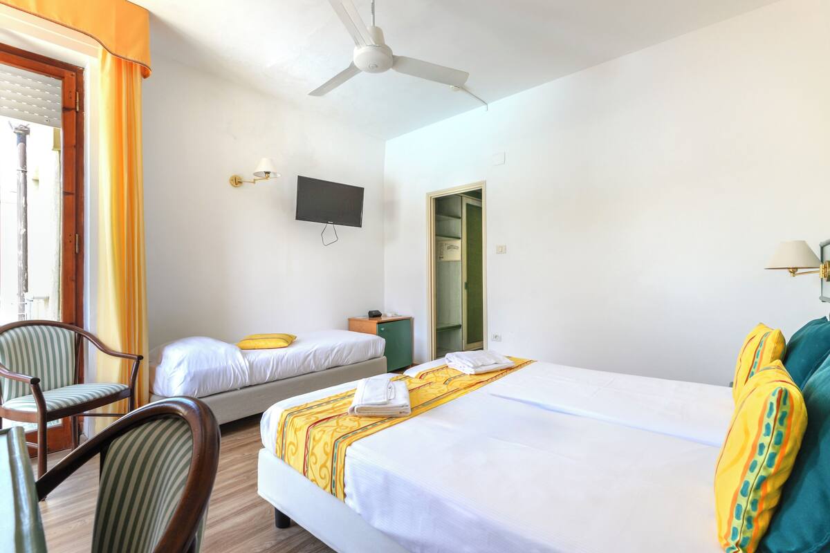 A hotel room with two beds, a chair, a television, a ceiling fan, and a window with curtains.