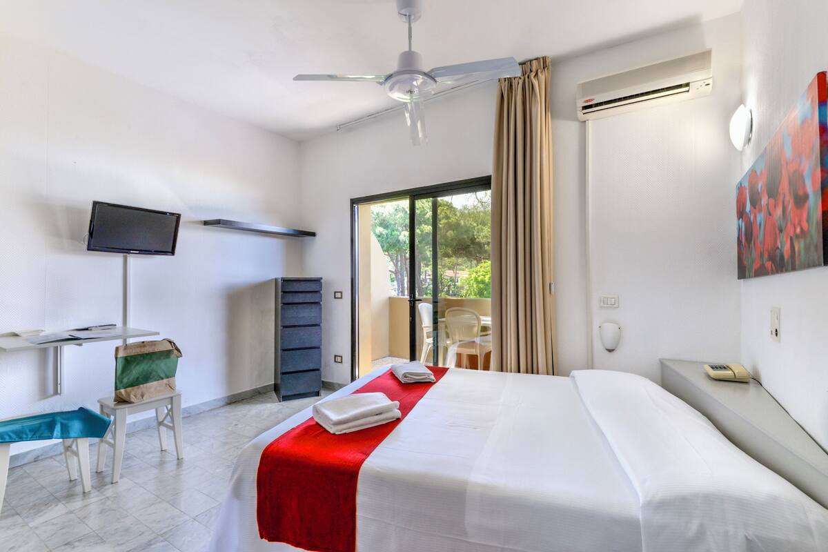 A hotel room with a bed, a desk with a computer, a TV, and a window with curtains.