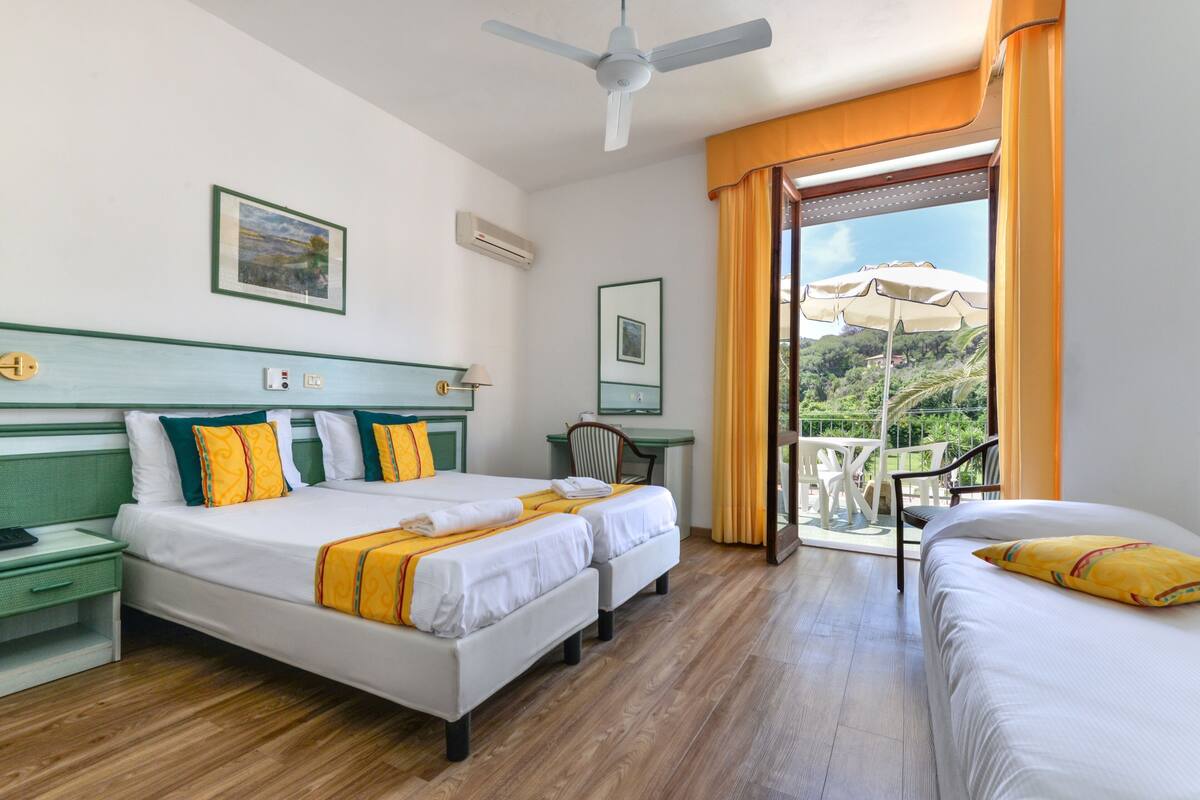 A hotel room with two beds, a desk, a chair, and a balcony with an umbrella.
