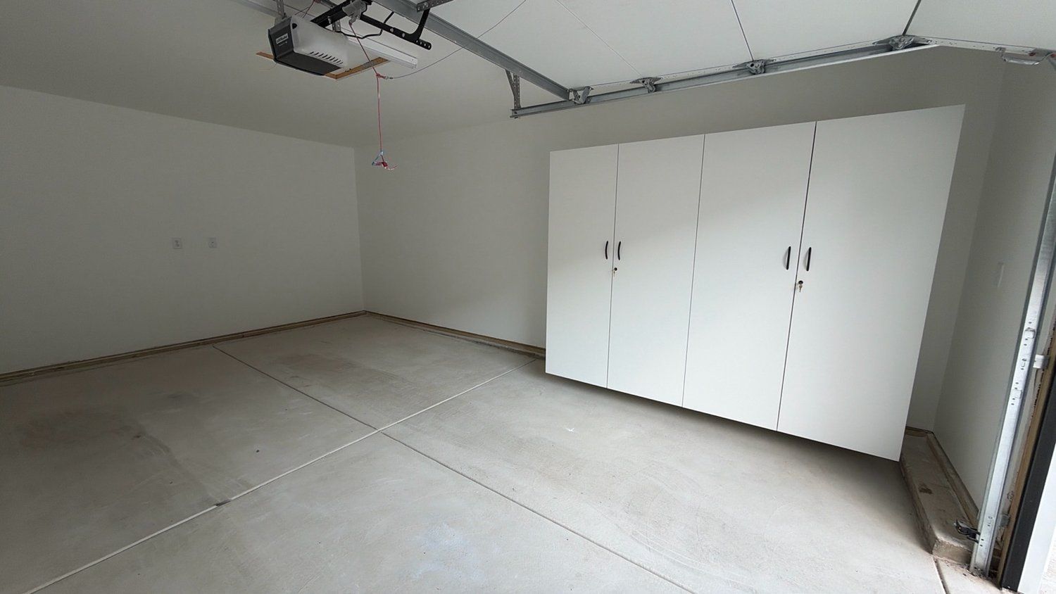 Una habitación con un amplio armario blanco, un proyector instalado en el techo y suelo de hormigón.