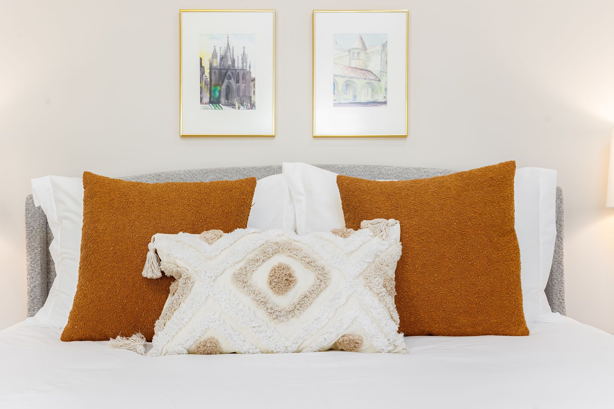 A bed with white and brown pillows, a white throw blanket, and two framed pictures on the wall.