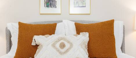 A bed with white and brown pillows, a white throw blanket, and two framed pictures on the wall.