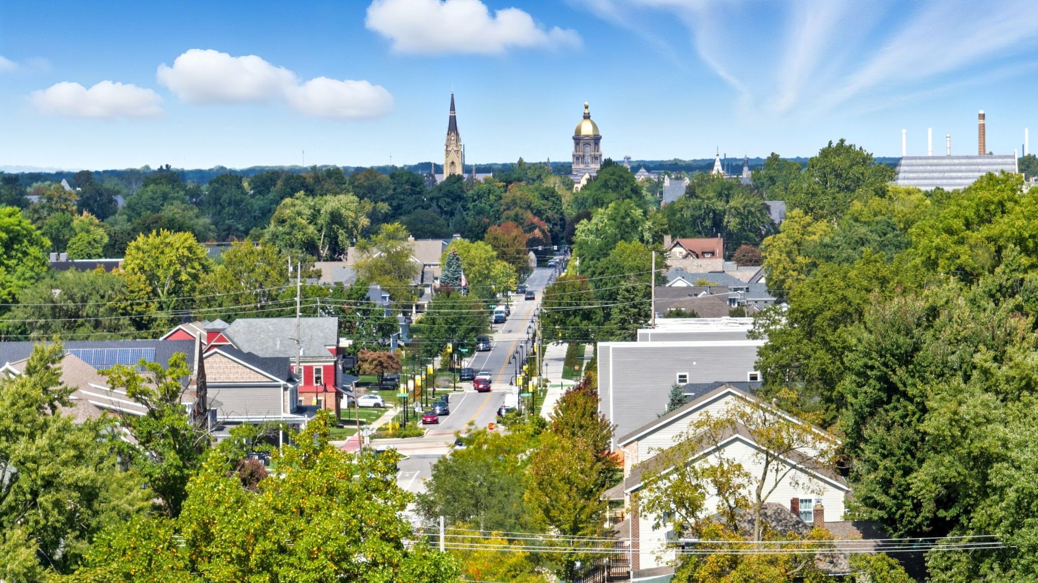 A town with a prominent church steeple and a large dome, surrounded by residential buildings and lush greenery.