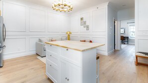 Une cuisine moderne avec des meubles blancs, un îlot central en bois et un lustre.