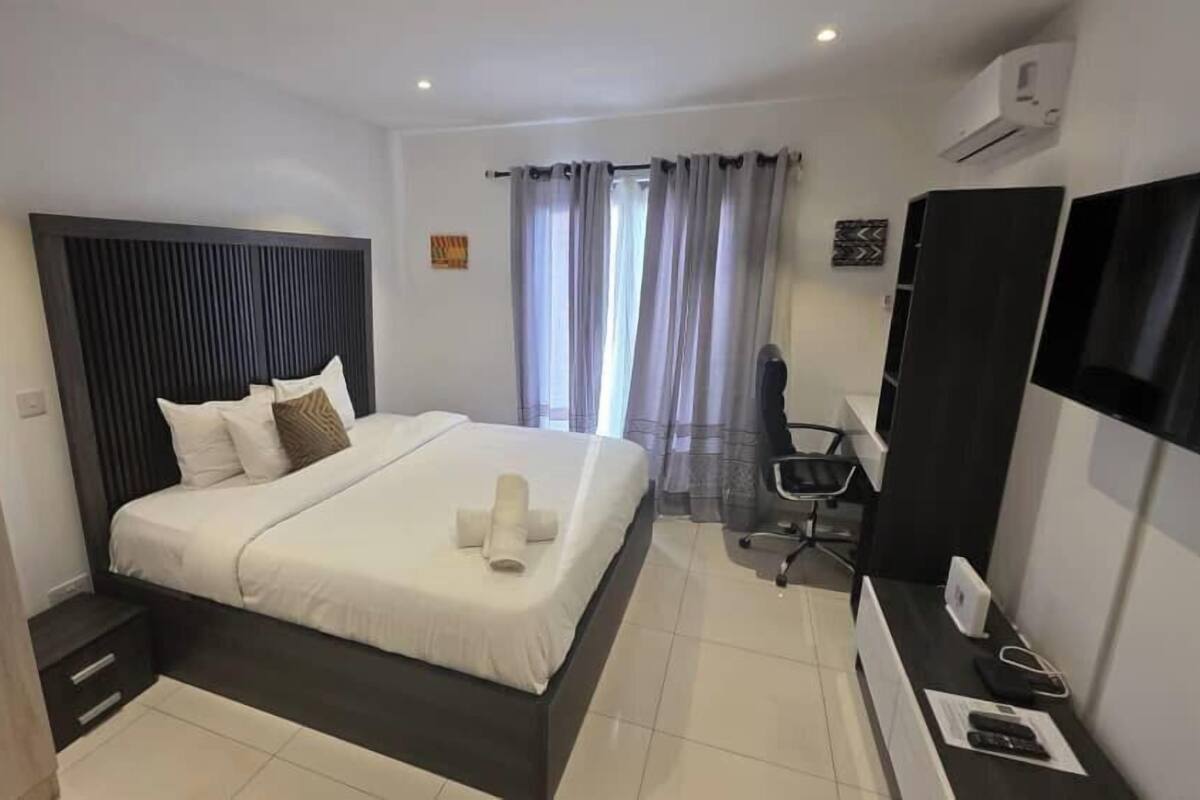 A modern hotel room with a large bed, a desk with a chair, a flat-screen TV, and a window with curtains.