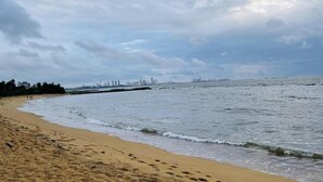 A beach with a sandy shore, a view of the ocean, and distant city skyline.