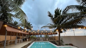 A pool area with a covered seating area, palm trees, and string lights.