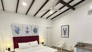 A modern bedroom with a large bed, a bench, a desk, and artwork on the walls.