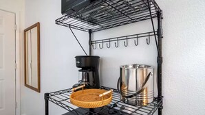 Ett kök med en svart metallhylla, en flätad korg, en kaffebryggare och en kastrull i rostfritt stål.