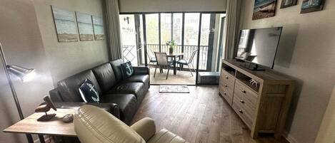 Una sala de estar con sofá, televisor, mesa de comedor y balcón con vistas.