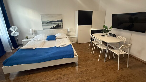 A modern hotel room with a bed, bedside table, lamp, fan, and a desk with chairs. - Smart 2BR Apt 10 Min from Westbahnhof (Vienna)