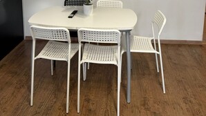 A dining area with a white table and four white chairs, a potted plant, and a flat-screen TV mounted on the wall. - Smart 2BR Apt 10 Min from Westbahnhof (Vienna)