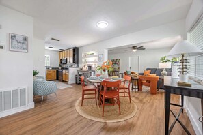 A modern kitchen with wooden cabinets, a dining area with a round table and chairs, and a living room with a sofa and a coffee table.