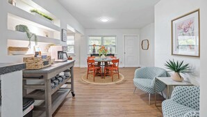 Una cocina moderna con comedor, piso de madera y estanterías empotradas con plantas.