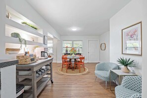 A modern kitchen with a dining area, wooden flooring, and built-in shelving with plants.