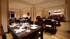 A spacious dining area with multiple tables set for dining, wooden pillars, and a kitchen area in the background. - Avianna Gangtok Prime Hotel & Spa  (Gangtok)