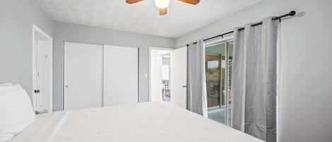 Un dormitorio con una cama grande, ventilador de techo y puerta corrediza de vidrio que da a un balcón.