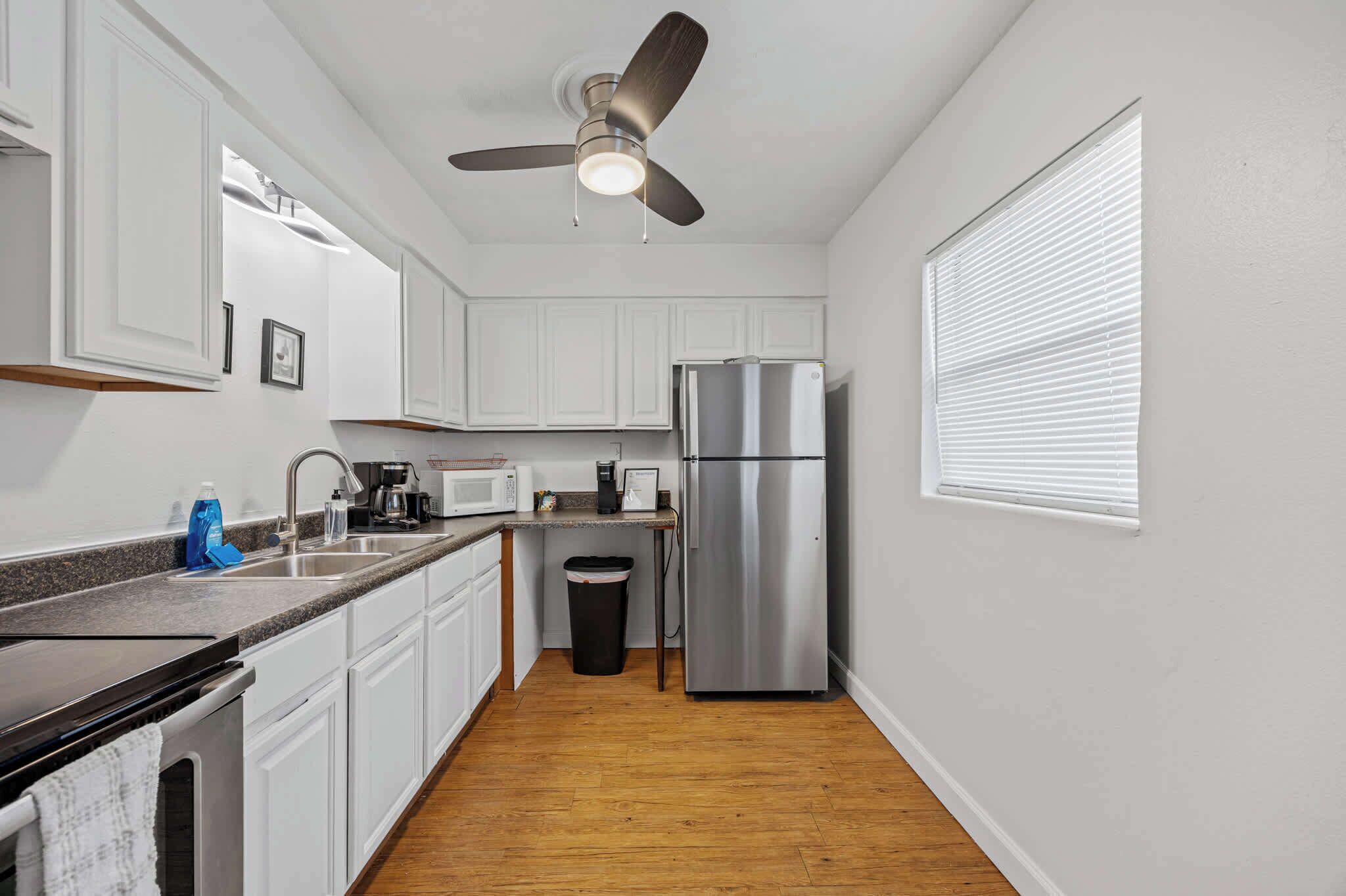 A compact kitchen with white cabinets, a stainless steel refrigerator, a microwave, and a ceiling fan.