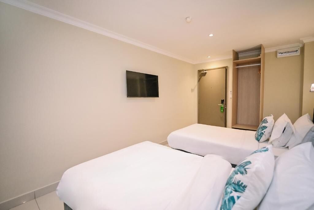 Habitación de hotel con dos camas individuales, un televisor montado en la pared y un armario de madera.