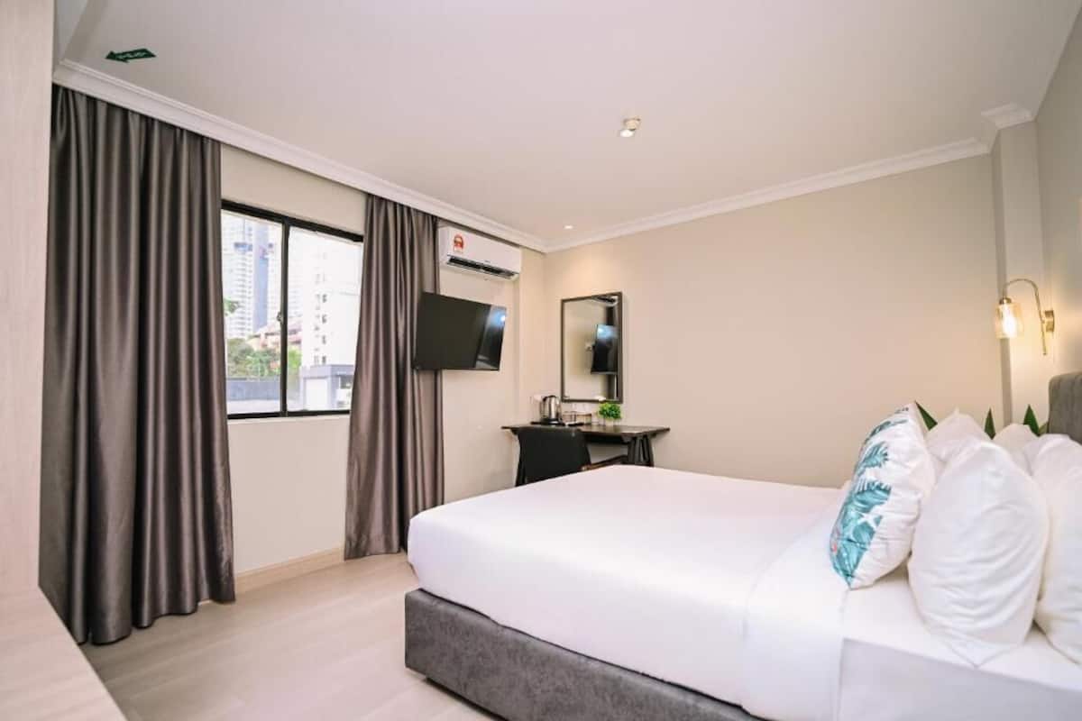 A hotel room with a large bed, a desk with a chair, a flat-screen TV, a mirror, and a window with curtains.
