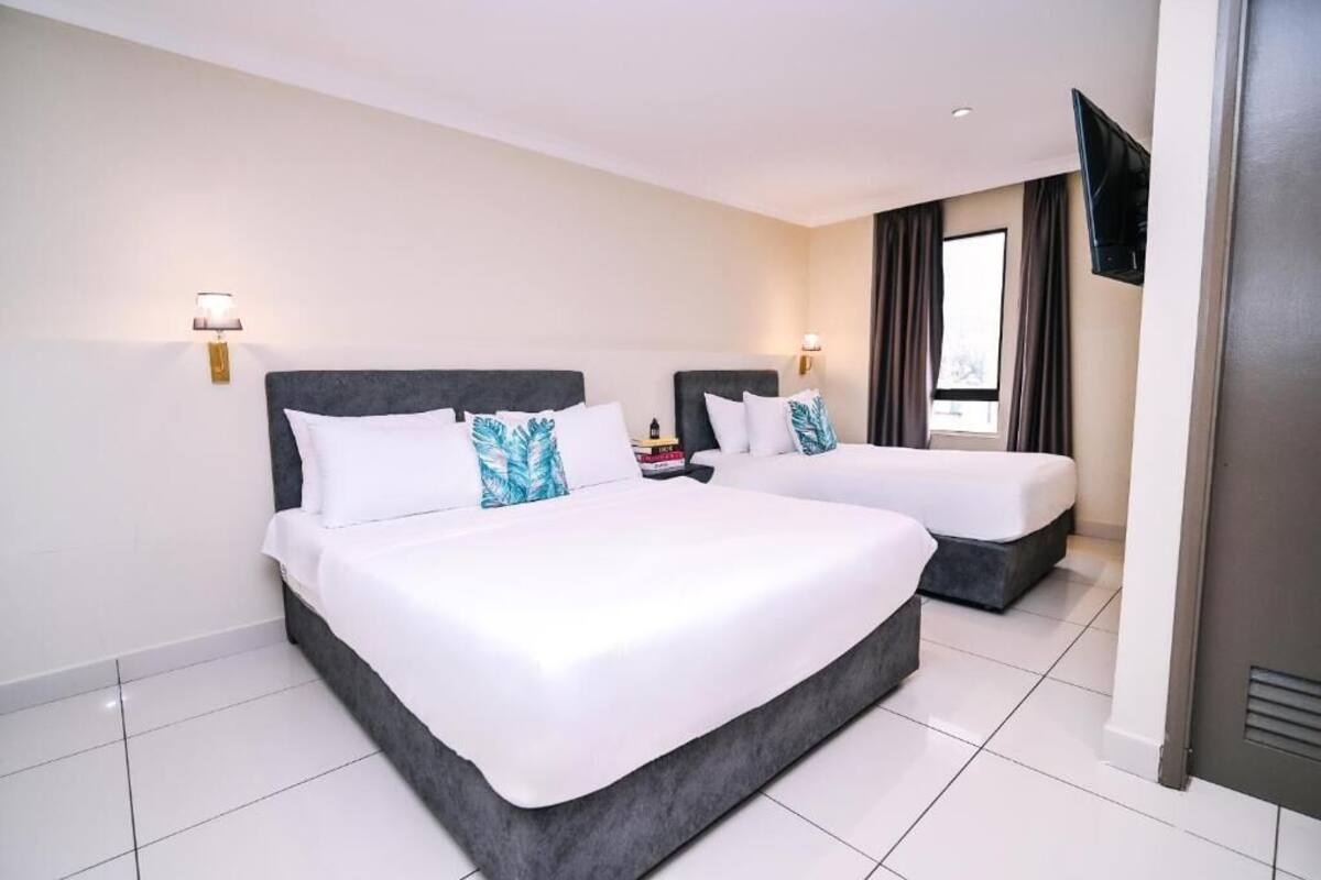 A hotel room with two beds, a flat-screen TV mounted on the wall, and a window with curtains.