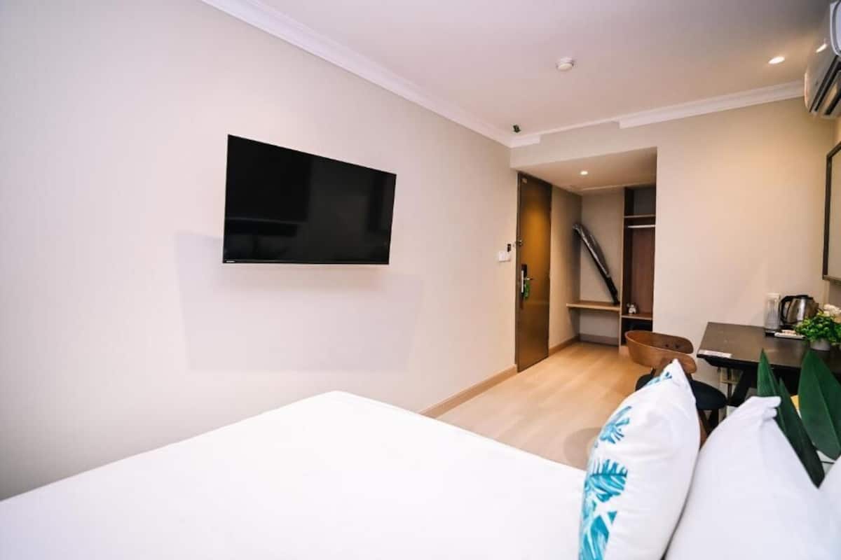 A modern hotel room with a flat-screen TV mounted on the wall, a bed with white bedding, a wooden floor, a staircase leading to a closet, and a small table with a plant.