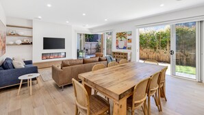 Een moderne woonkamer met een houten eettafel, banken en een flatscreen televisie.