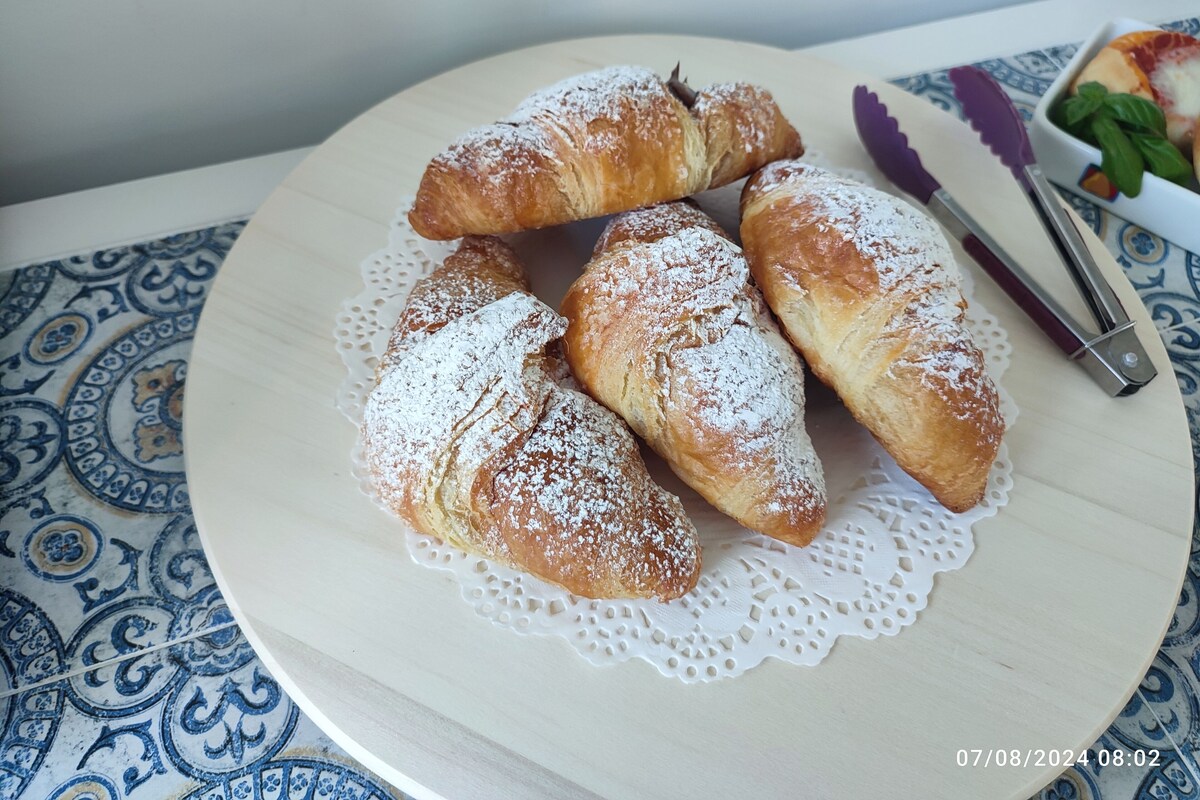 A plate of croissants on a doily with a knife and a bowl of greens on a table.