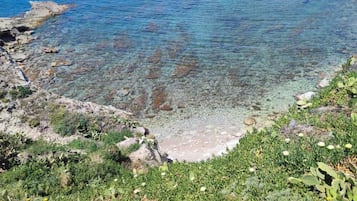 Paesaggio costiero con acque limpide, costa rocciosa e vegetazione verde.