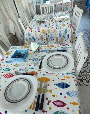 A dining table set with plates, cutlery, and glasses, covered with a tablecloth featuring a fish pattern. - Tramonti d' alba bed and breakfast (Terrasini)