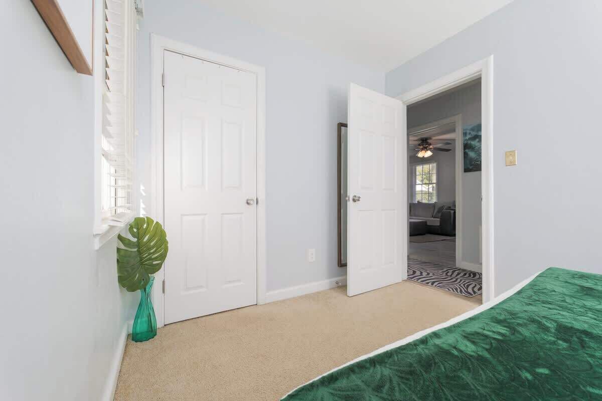 A bedroom with a green bedspread, a white door, and a plant in a green vase.