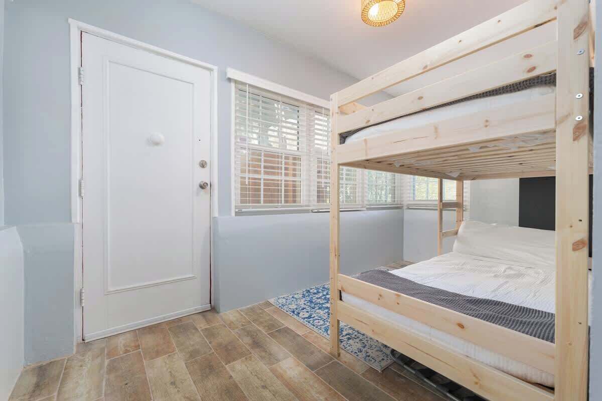 A room with a bunk bed, a door, a window with blinds, and a patterned rug.