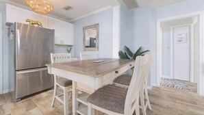 Une cuisine moderne avec un réfrigérateur en acier inoxydable, une table à manger en bois, des chaises blanches et un lustre.