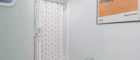 Um banheiro com cortina de chuveiro, porta-papel higiênico e um quadro com pôster de avião.