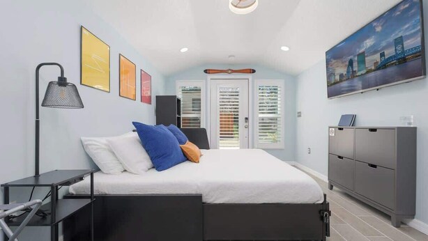 Une chambre à coucher avec un lit, un bureau, une chaise, une armoire et un tableau accroché au mur.