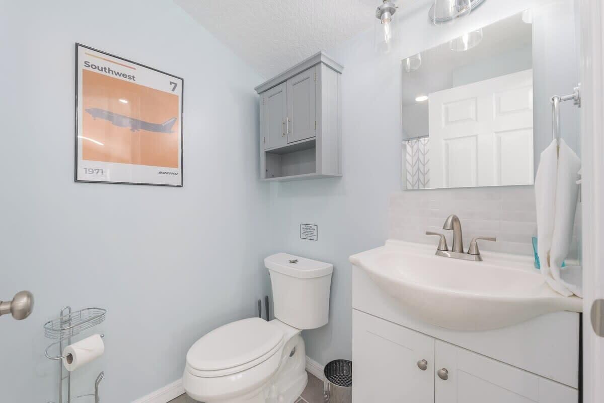 A bathroom with a toilet, a sink, a mirror, a cabinet, and a poster on the wall.
